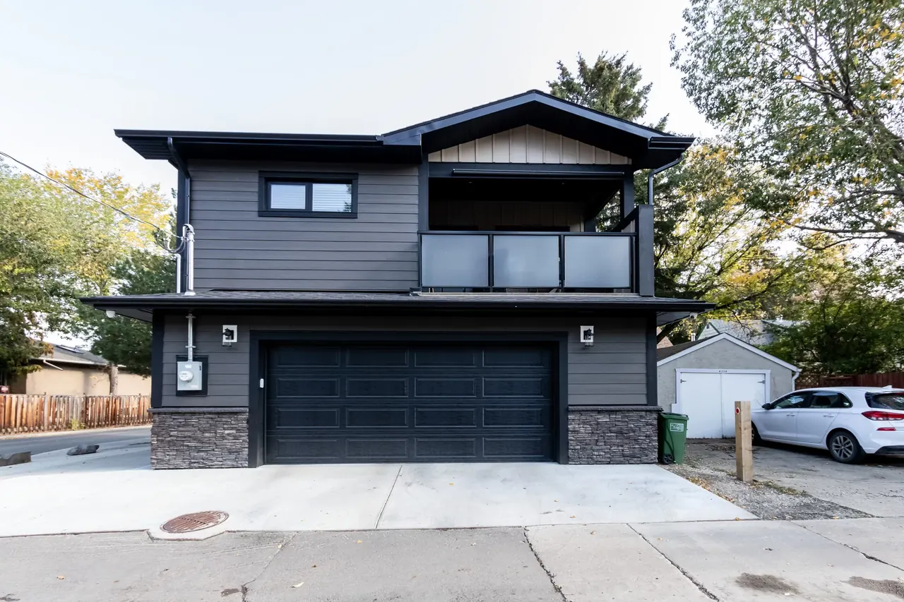 Two-storey garage suite with charcoal siding and a stone base, seen from the lane