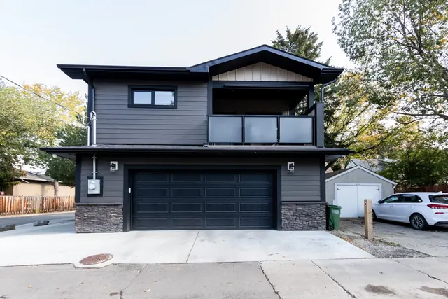 Two-storey garage suite with charcoal siding and a stone base, seen from the lane